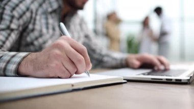 Masanın üzerine çeşitli eşyalarla birlikte bir deftere yazı yazan erkek elleri yakın plan.