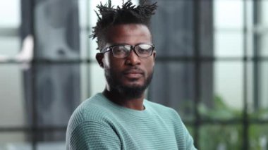 Gözlüklü kendine güvenen siyah işadamı ciddi bir ifadeyle kameraya bakıyor.