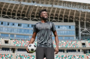 Kendine güvenen siyah futbolcu topu elinde tutuyor.