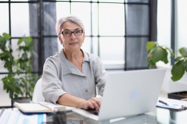 Smiling 60-year-old business womanusing a computer at office