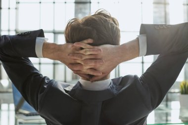 İşçi ofiste elleri başının arkasında oturur ve pencereden dışarı bakar.