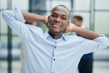 Happy african american young businessman holding hands behind head looking at camera