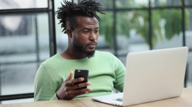 Siyahi işadamı ofiste cep telefonuyla konuşuyor.