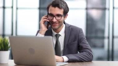 Ofiste akıllı telefondan konuşan mutlu genç işadamı.