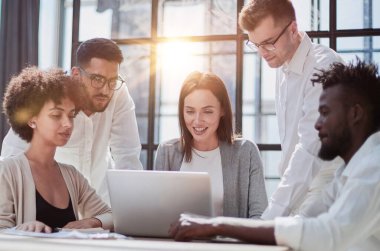 Çevrimiçi projeyi tartışan mutlu genç bayan çalışan, gözlüklü yetenekli takım liderine bilgisayar sunumu yapıyor. Uygulamaları kullanarak laptopta çift olarak çalışan dost canlısı meslektaşlar.