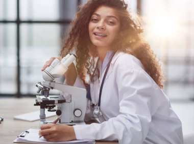 Çekici kadın bilim adamı mikroskoptan bakıyor.