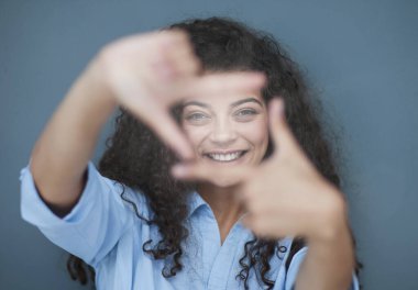 Neşeli, kendinden emin, katlanmış kolları olan bir kadının fotoğrafı. Mavi gömlek, gri arka plan.