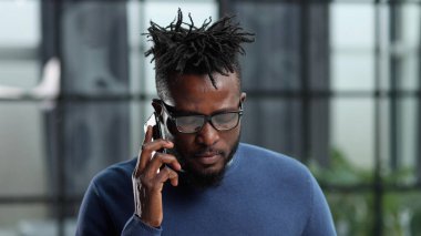 İletişim ve teknoloji danışmanı Afro-Amerikan iş adamı ofisteki akıllı telefondan arıyor.