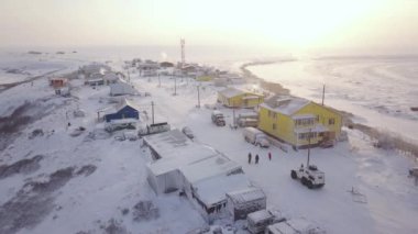 Bulutlu bir gökyüzünün altında binalar, ağaçlar ve beyaz manzaralı karla kaplı küçük bir kasabanın hava manzarası sakin bir kış manzarası yaratıyor.