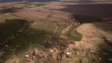 Yeşiller yemyeşil çimenler, dağınık ağaçlar ve uzaktaki birkaç ev ile doğal bir manzara, yukarıdan huzurlu ve resimsel bir manzara yaratıyor.