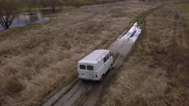 Beyaz bir minibüsü görüntüleyen bir hava perspektifi manzaralı bir arazide toprak bir yol boyunca uzanan yemyeşil çimenler ve görünürde demiryolu ya da toplu taşımacılık yok.