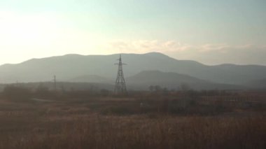 Bulutlu bir gökyüzünün altında arka planda dağlar olan uçsuz bucaksız bir tarlayı çeken puslu bir fotoğraf. Doğal manzara ağaçlar ve elektrik direğiyle vurgulanır ve dingin atmosfere eklenir.