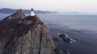 Okyanus kıyısındaki kayalık bir uçuruma tünemiş bir deniz feneri aşağıdaki su, gökyüzü ve doğal manzaranın nefes kesici bir hava manzarasını sunuyor.