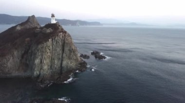 Denizin üzerindeki engebeli bir uçuruma tünemiş deniz fenerinin hava perspektifi, su, gökyüzü ve doğal manzaralarla çevrili.