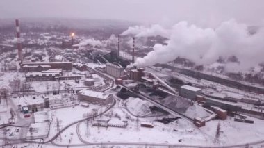 Kar örtüsü altında bir fabrikanın kuş bakışı görüntüsü bacalardan yükselen dumanlar bulutlu gökyüzüne karışıyor.