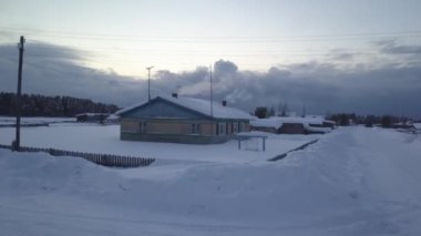 Karla kaplı bir tarlada, sakin bir kış harikalar diyarı yaratan, sakin bir atmosferi ve manzaralı bir evi gösteren manzaralı bir video.
