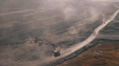 Tozlu yollarda malzeme taşıyan kamyonlarla dolu geniş bir maden sahası ve dağınık enkaz parçaları..