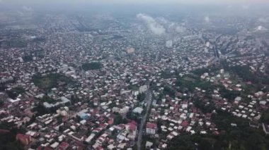 Uçsuz bucaksız gökyüzünün altında ağaçlar ve yollarla çevrili çok sayıda bina ve kule bloğunun yer aldığı bir şehir manzarası.