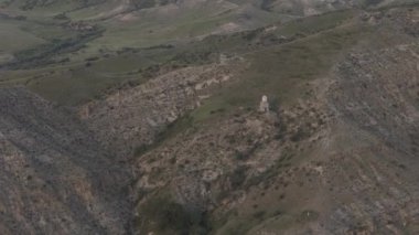 Havadan bakıldığında, kayan tepeler, derin vadiler ve ıssız bir yapı ile çarpıcı bir manzara görülüyor.