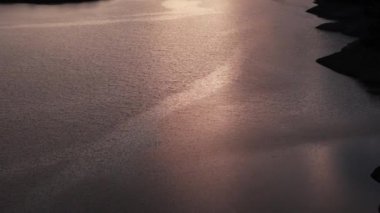 Sakin bir nehir, engebeli araziyle çevrili çarpıcı bir günbatımının sıcak parıltısını nazikçe yansıtıyor.