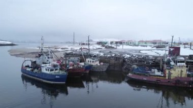 Huzurlu ve sakin bir kış sahnesinde, karlı bir limana güvenli bir şekilde yanaşmış balıkçı tekneleri görülüyor. Arktik Köy Teriberka, Kola Yarımadası, Rusya