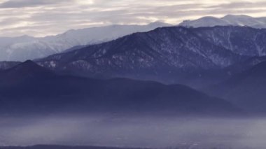 Sisli bir dağ sırasının ve bulutlu gökyüzünün çarpıcı manzarası, doğayı, sükuneti ve cazibeyi yakalıyor.