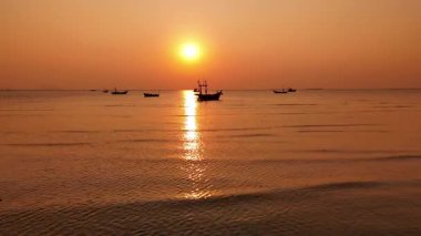 Akşamları Tayland 'da sakin sularda yüzen balıkçı tekneleriyle sakin bir günbatımı sahnesi.