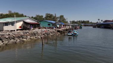 Tayland rıhtımında stilt evler, balıkçı tekneleri ve sakin sular yer alıyor..