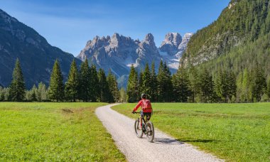 Toblach ve Cortina Dampezzo, Three Peaks Dolomites, South Tirol, İtalya arasındaki Hoehlenstein vadisinde eski bir demiryolu setinde elektrikli dağ bisikletine binen hoş ve aktif yaşlı bir kadın.