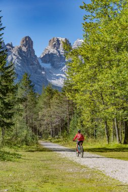 Toblach ve Cortina Dampezzo, Three Peaks Dolomites, South Tirol, İtalya arasındaki Hoehlenstein vadisinde eski bir demiryolu setinde elektrikli dağ bisikletine binen hoş ve aktif yaşlı bir kadın.