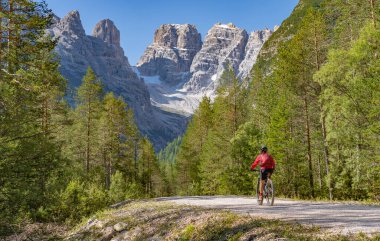 Toblach ve Cortina Dampezzo, Three Peaks Dolomites, South Tirol, İtalya arasındaki Hoehlenstein vadisinde eski bir demiryolu setinde elektrikli dağ bisikletine binen hoş ve aktif yaşlı bir kadın.