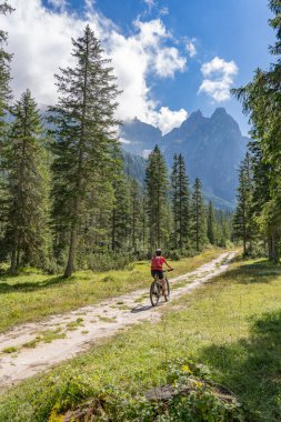 Arka planda Sexten Dolomites nükteli Fischlein Vadisi 'nde bisiklete binen son sınıf güzel bir kadın, Tre cime Ulusal Parkı, Güney Tirol, İtalya 