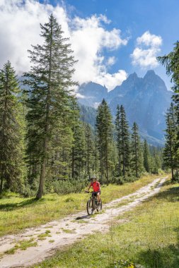 Arka planda Sexten Dolomites nükteli Fischlein Vadisi 'nde bisiklete binen son sınıf güzel bir kadın, Tre cime Ulusal Parkı, Güney Tirol, İtalya 