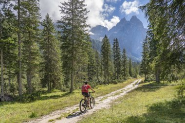 Arka planda Sexten Dolomites nükteli Fischlein Vadisi 'nde bisiklete binen son sınıf güzel bir kadın, Tre cime Ulusal Parkı, Güney Tirol, İtalya 