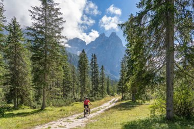 Arka planda Sexten Dolomites nükteli Fischlein Vadisi 'nde bisiklete binen son sınıf güzel bir kadın, Tre cime Ulusal Parkı, Güney Tirol, İtalya 
