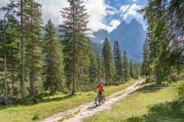 Arka planda Sexten Dolomites nükteli Fischlein Vadisi 'nde bisiklete binen son sınıf güzel bir kadın, Tre cime Ulusal Parkı, Güney Tirol, İtalya 