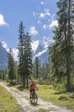 Arka planda Sexten Dolomites nükteli Fischlein Vadisi 'nde bisiklete binen son sınıf güzel bir kadın, Tre cime Ulusal Parkı, Güney Tirol, İtalya 