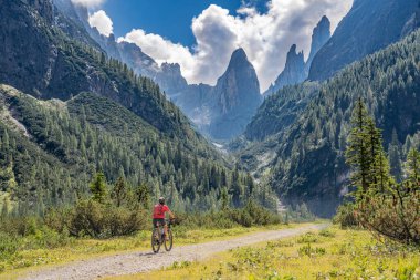 Arka planda Sexten Dolomites nükteli Fischlein Vadisi 'nde bisiklete binen son sınıf güzel bir kadın, Tre cime Ulusal Parkı, Güney Tirol, İtalya 
