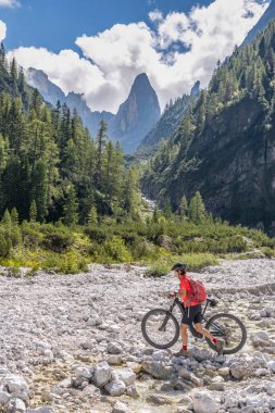 Arka planda Sexten Dolomites nükteli Fischlein Vadisi 'nde bisiklete binen son sınıf güzel bir kadın, Tre cime Ulusal Parkı, Güney Tirol, İtalya 