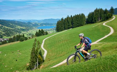 Steibis, Bavyera, Almanya yakınlarındaki Allgau ve Bregenz Ormanları 'nın muhteşem manzarasının tadını çıkaran, elektrikli dağ bisikletine binen son sınıf güzel bir kadın.