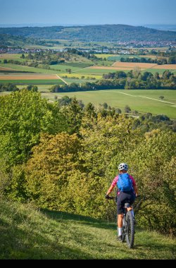 Swabian Albleri 'nin altın renkli sonbahar ormanlarında elektrikli dağ bisikletine binen hoş, aktif yaşlı bir kadın.