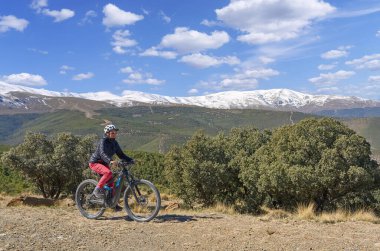 Granada, Anslusia, İspanya yakınlarındaki İspanyol Sierra Nevada 'nın karlı dağlarının altında elektrikli dağ bisikletiyle bisiklet süren hoş, aktif, son sınıf öğrencisi bir kadın.