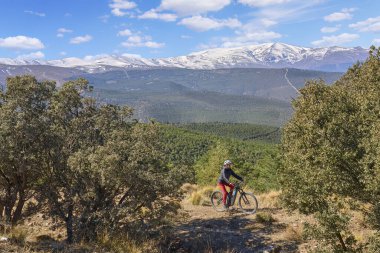 Granada, Anslusia, İspanya yakınlarındaki İspanyol Sierra Nevada 'nın karlı dağlarının altında elektrikli dağ bisikletiyle bisiklet süren hoş, aktif, son sınıf öğrencisi bir kadın.