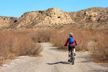 Almeria, Andlusia, İspanya yakınlarındaki Tabernas çölünde, elektrikli dağ bisikletiyle gezen hoş, aktif, son sınıf öğrencisi bir kadın.