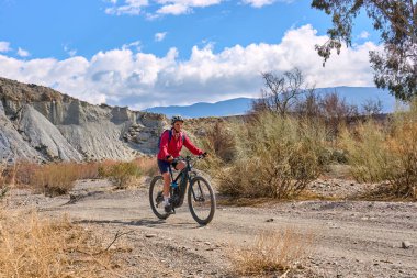 Almeria, Andlusia, İspanya yakınlarındaki Tabernas çölünde, elektrikli dağ bisikletiyle gezen hoş, aktif, son sınıf öğrencisi bir kadın.