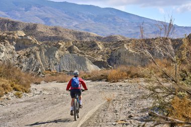 Almeria, Andlusia, İspanya yakınlarındaki Tabernas çölünde, elektrikli dağ bisikletiyle gezen hoş, aktif, son sınıf öğrencisi bir kadın.
