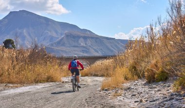 Almeria, Andlusia, İspanya yakınlarındaki Tabernas çölünde, elektrikli dağ bisikletiyle gezen hoş, aktif, son sınıf öğrencisi bir kadın.