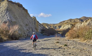Almeria, Andlusia, İspanya yakınlarındaki Tabernas çölünde, elektrikli dağ bisikletiyle gezen hoş, aktif, son sınıf öğrencisi bir kadın.