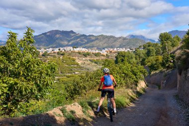 İspanya 'nın Endülüs kenti Nerja yakınlarındaki Frigiliana beyaz köyünde elektrikli dağ bisikletiyle bisiklet süren hoş bir son sınıf öğrencisi.