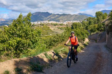 İspanya 'nın Endülüs kenti Nerja yakınlarındaki Frigiliana beyaz köyünde elektrikli dağ bisikletiyle bisiklet süren hoş bir son sınıf öğrencisi.